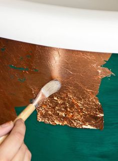 a person is painting copper foil on the bottom of a white bowl with a brush