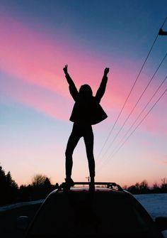 a woman standing on top of a car in front of a pink and blue sky