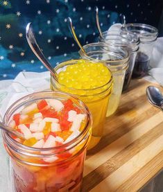 four jars filled with food sitting on top of a wooden cutting board next to spoons