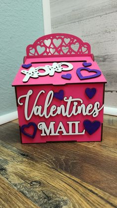 a valentine's mail box with hearts and cutouts on the top, sitting on a wooden table