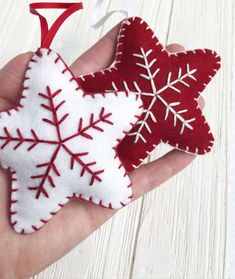 a hand is holding two red and white felt snowflake ornament ornaments