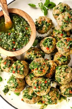 a white plate topped with meatballs covered in pesto sauce and a wooden spoon