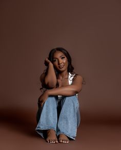 a young woman sitting on the ground with her legs crossed and looking at the camera