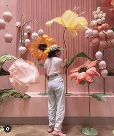 a woman standing in front of a pink wall with paper flowers on it and other decorations behind her