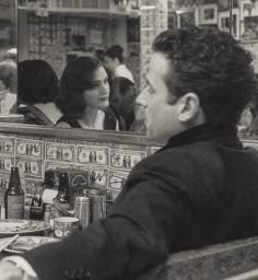 a man sitting at a table in front of a mirror next to a woman eating food