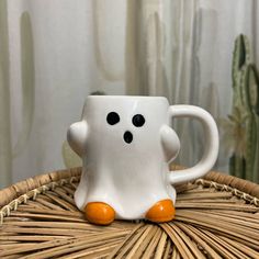 a white coffee cup sitting on top of a wicker table next to a cactus