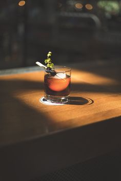 a small glass filled with liquid sitting on top of a wooden table next to a window