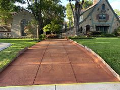 an empty driveway in front of a house with trees and grass on both sides of it