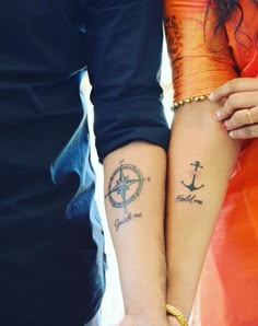 two people holding hands with tattoos on their arms and one has a compass tattooed on the arm