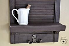 a white mug sitting on top of a wooden shelf next to a wall mounted hook