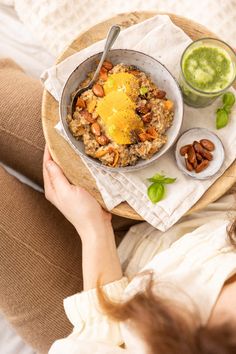 a woman holding a bowl of oatmeal with nuts and green smoothie