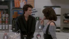 the young man and woman are talking to each other in front of a vending machine