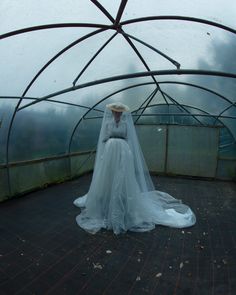 a woman in a white wedding dress and veil standing under an overhanging structure