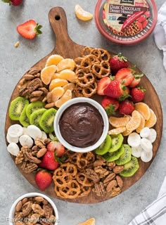 a platter filled with fruit, nuts and chocolate dip surrounded by pretzels