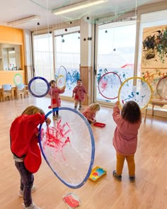 three children are playing with plastic discs in a room filled with wooden floors and large windows