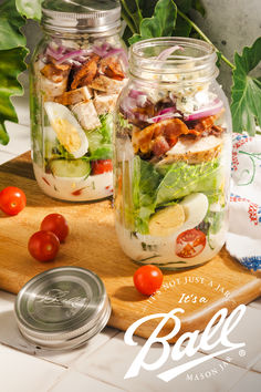 two mason jars filled with salads on top of a cutting board