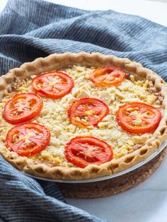 an uncooked pie with tomatoes on top sitting on a blue towel next to it