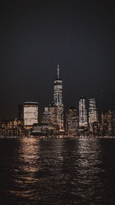 the city skyline is lit up at night with lights reflecting off the water in front of it