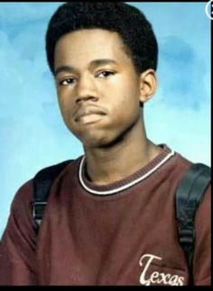 a young man in a maroon shirt is posing for a photo with his hand on his hip