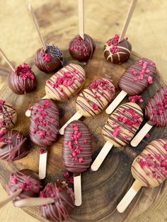 chocolate covered desserts on sticks with sprinkles and pink frosting sitting on a wooden plate