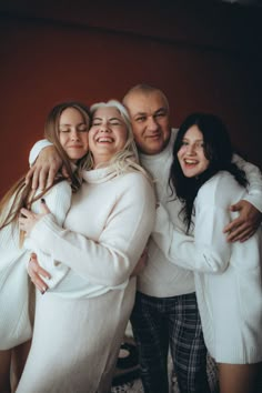 three people hugging each other in front of a red wall with their arms around one another