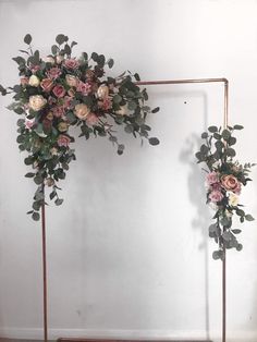 an arch decorated with flowers and greenery in front of a white wall on a wooden floor