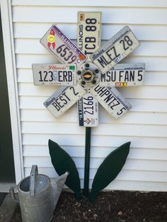 a flower made out of license plates on the side of a house with a watering can next to it