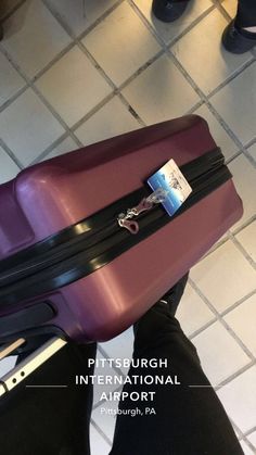 a purple suitcase sitting on top of a tiled floor next to a persons legs and feet