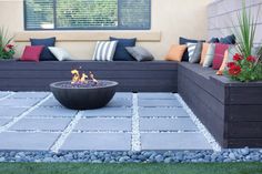 a fire pit sitting in the middle of a patio surrounded by plants and pillows on top of it