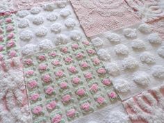 a close up of a pink and white quilt on a bed with crocheted flowers