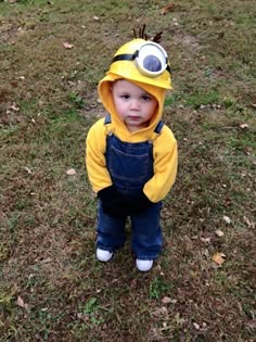 a little boy dressed in a minion costume standing on the grass wearing overalls