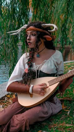 a woman sitting on the ground with a guitar in her hand and horns around her head