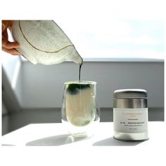 a person pouring some liquid into a glass next to a container on a white table