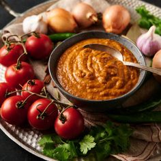 a bowl of tomato hummus next to some tomatoes and garlic on a platter