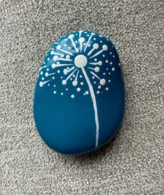 a painted rock with a dandelion design on it sitting on the floor next to a gray carpet