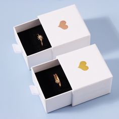 two white boxes with gold rings in them on a blue surface, one opened and the other closed