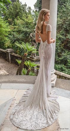 the back of a woman's wedding dress, with trees in the background and bushes on either side