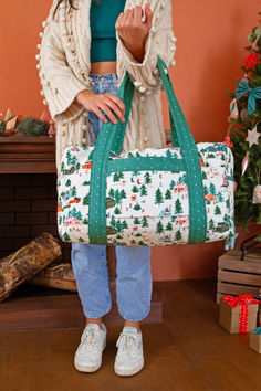 a woman standing in front of a christmas tree holding a duffel bag with trees on it