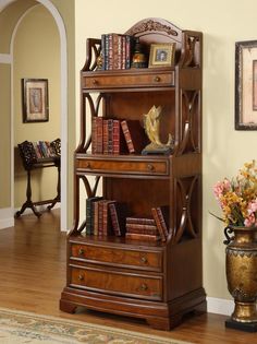 a wooden book shelf with books on top of it in a living room next to a vase filled with flowers