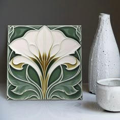 a white vase sitting on top of a table next to a ceramic wall art piece