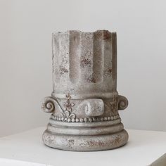 an old white vase sitting on top of a table in front of a white wall