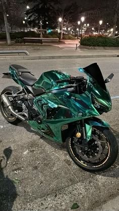 a shiny green motorcycle parked on the side of the road at night with street lights in the background