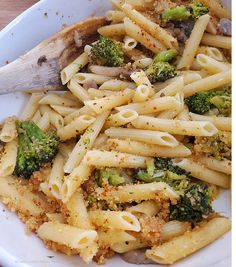 pasta with broccoli and parmesan cheese on a white plate next to a wooden spoon