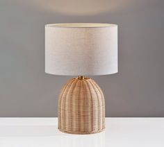 a wicker lamp on a white table with a beige linen shade over the top