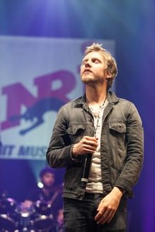 a man standing on top of a stage with his hands in his pockets while holding a microphone