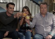 three people sitting on a couch holding drinks