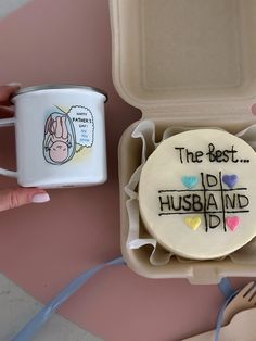 someone is holding a coffee mug next to a decorated cookie in a foam container that says the best husband and dad