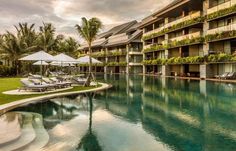 an outdoor swimming pool with lounge chairs and umbrellas in front of the resort building