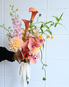 a person holding a bouquet of flowers against a white brick wall in front of the camera