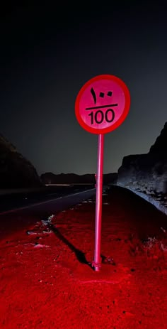 a red street sign sitting on the side of a road next to a mountain at night